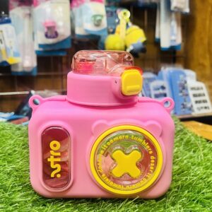 Home Front view of closed cute camera shape kids water bottle with silicone straw in pink standing on green grass