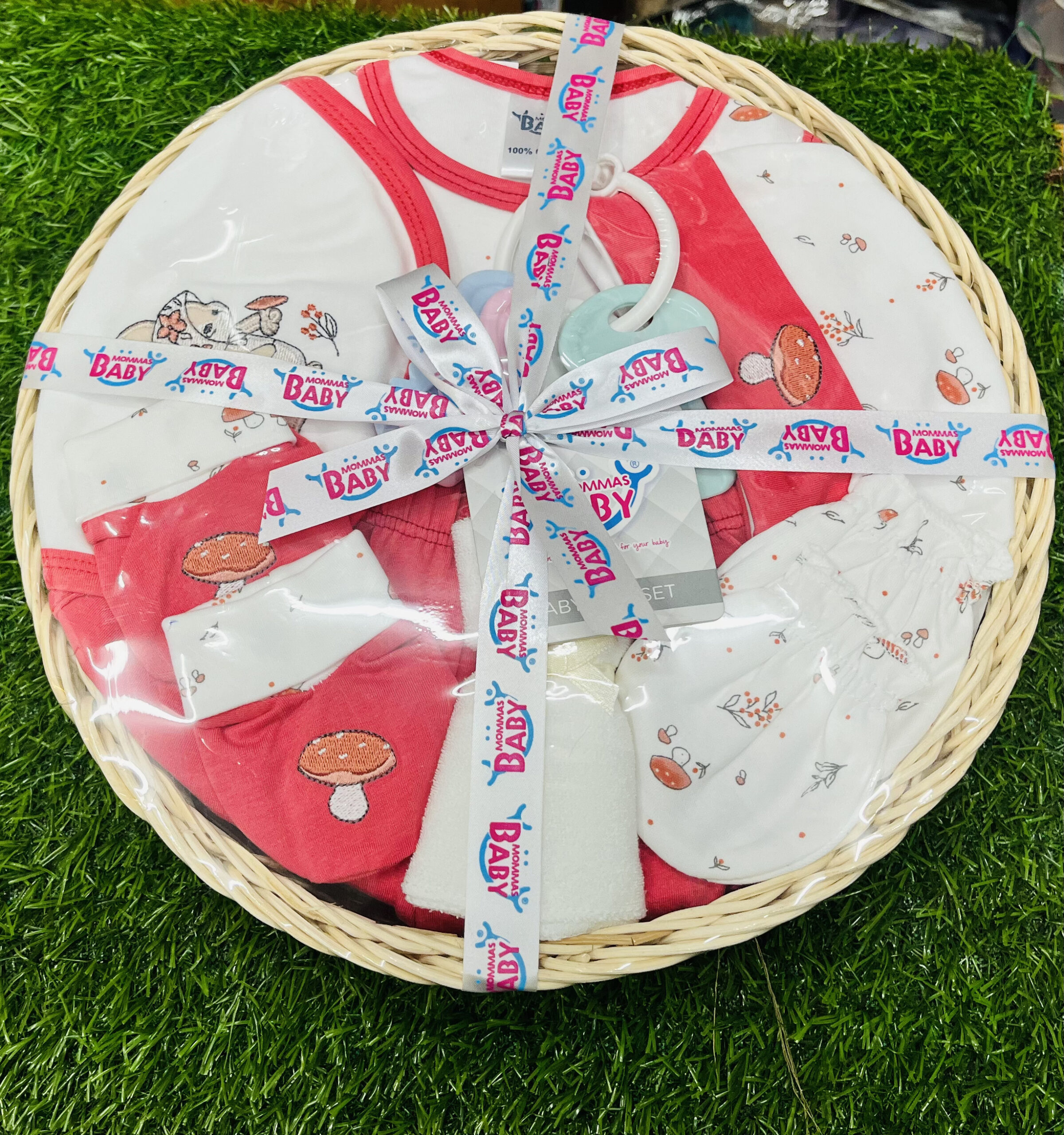 mommas baby 10 pcs newborn baby gift basket set – 100% cotton with rattle (coral pink) Mommas Baby 10 pcs newborn baby gift basket set top view in clear gift wrap with ribbon on green grass